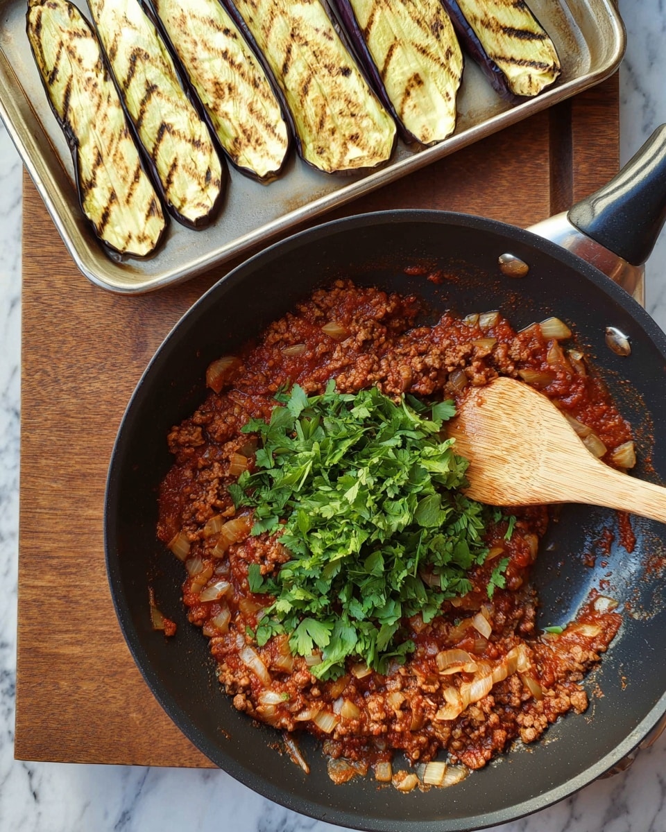 A black frying pan sits on a wooden board with a cooked meat sauce inside, which is reddish-brown with small meat pieces and visible chopped onions mixed in. On top of the sauce, there is a pile of fresh green parsley leaves in the center. A wooden spoon with a light brown handle rests inside the pan on the sauce. Behind the pan is a metal baking tray holding several slices of grilled eggplant, each slice showing charred grill marks and pale yellow and purple colors. The background is a white marbled surface. Photo taken with an iphone --ar 4:5 --v 7